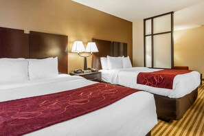 Quarto de hotel com duas camas, uma mesa de cabeceira com abajur e uma janela grande.