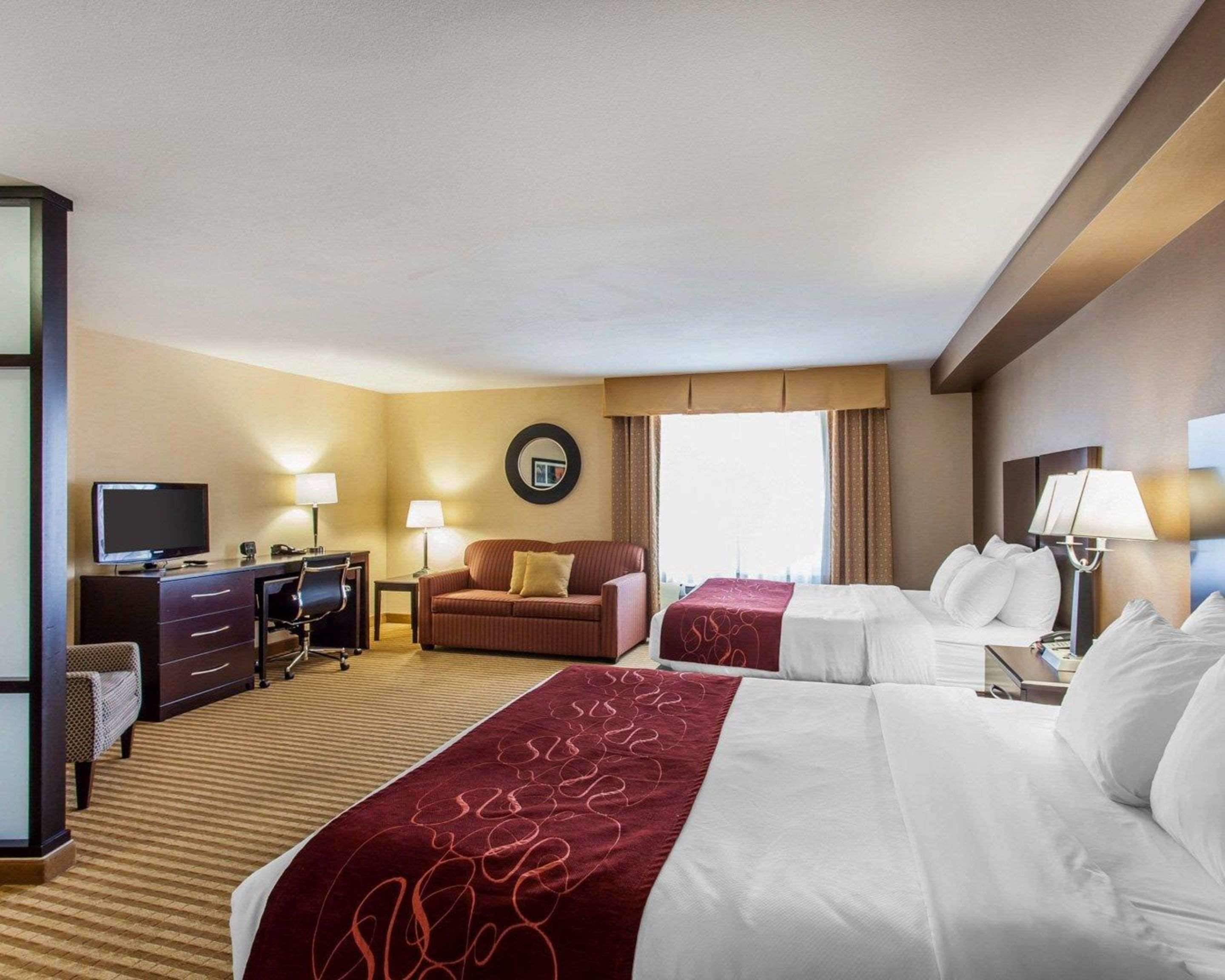 A hotel room with two beds, a desk, a television, and a circular mirror on the wall.