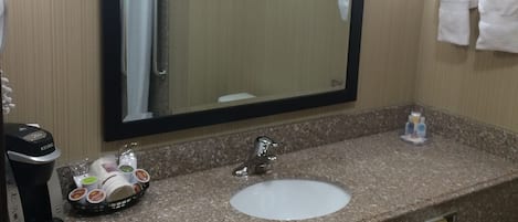 A hotel bathroom with a granite countertop, a sink, a mirror, a framed picture on the wall, and a towel rack.