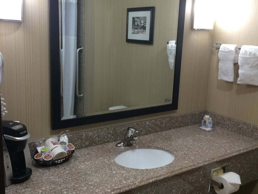 A hotel bathroom with a granite countertop, a sink, a mirror, a framed picture on the wall, and a towel rack.
