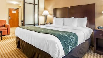 A hotel room with a large bed, a desk, a chair, a lamp, and a door.