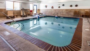 Piscina interna com superfície de água cristalina, rodeada por espreguiçadeiras e uma parede de azulejos decorada com peixes.