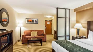A hotel room with a bed, a sofa, a coffee table, a desk with a computer, a mirror, a lamp, and a door.