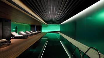 Una piscina interior moderna con un solárium de madera y sillones de descanso.