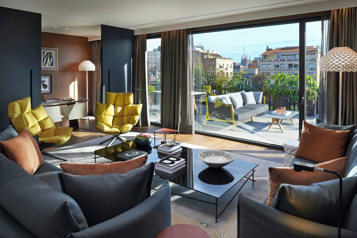 Una sala de estar moderna con sofá, sillones, una mesa de centro y vistas de la ciudad a través de amplios ventanales.