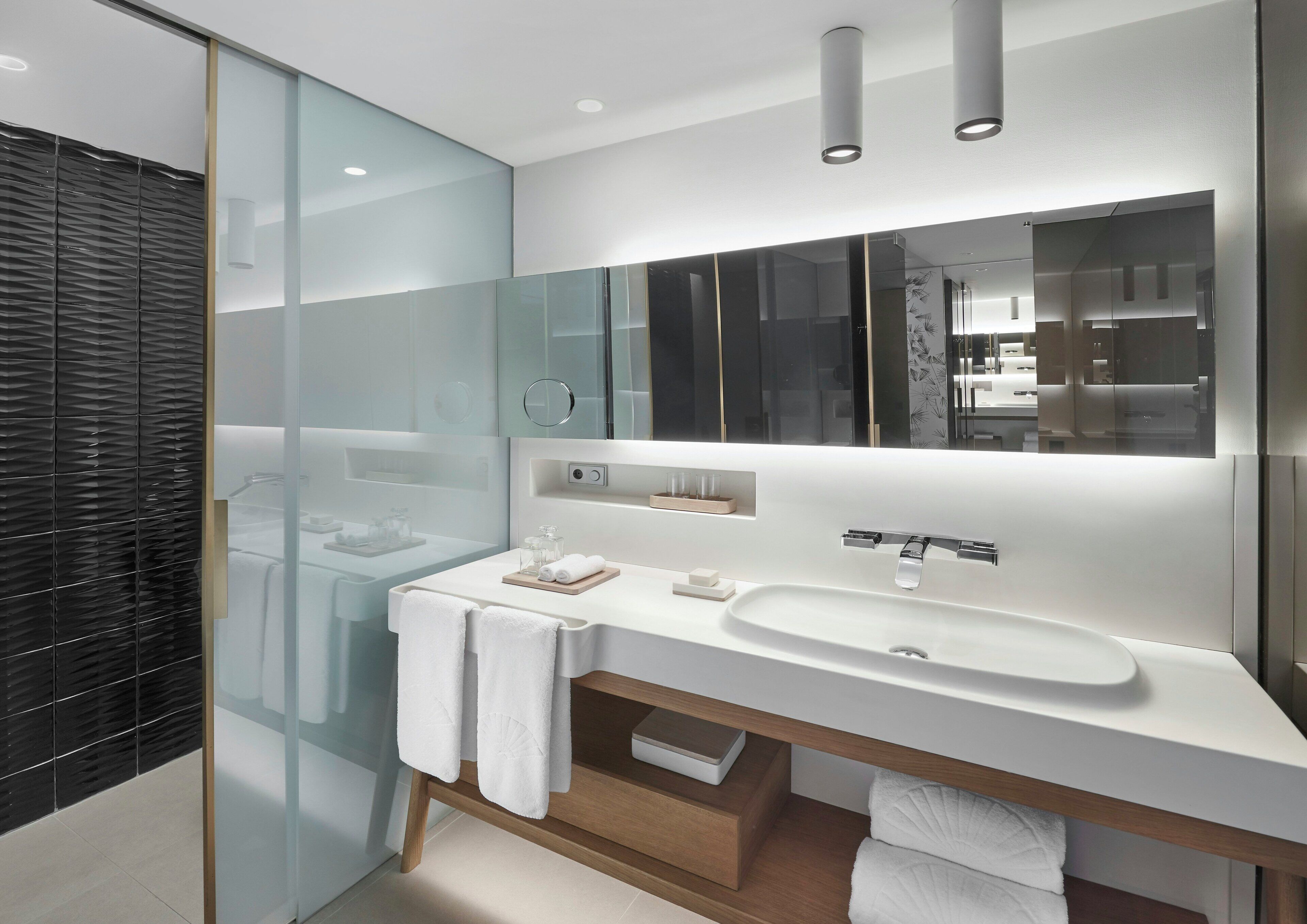 Un baño moderno con cabina de ducha de vidrio, un lavabo blanco y un espejo grande.