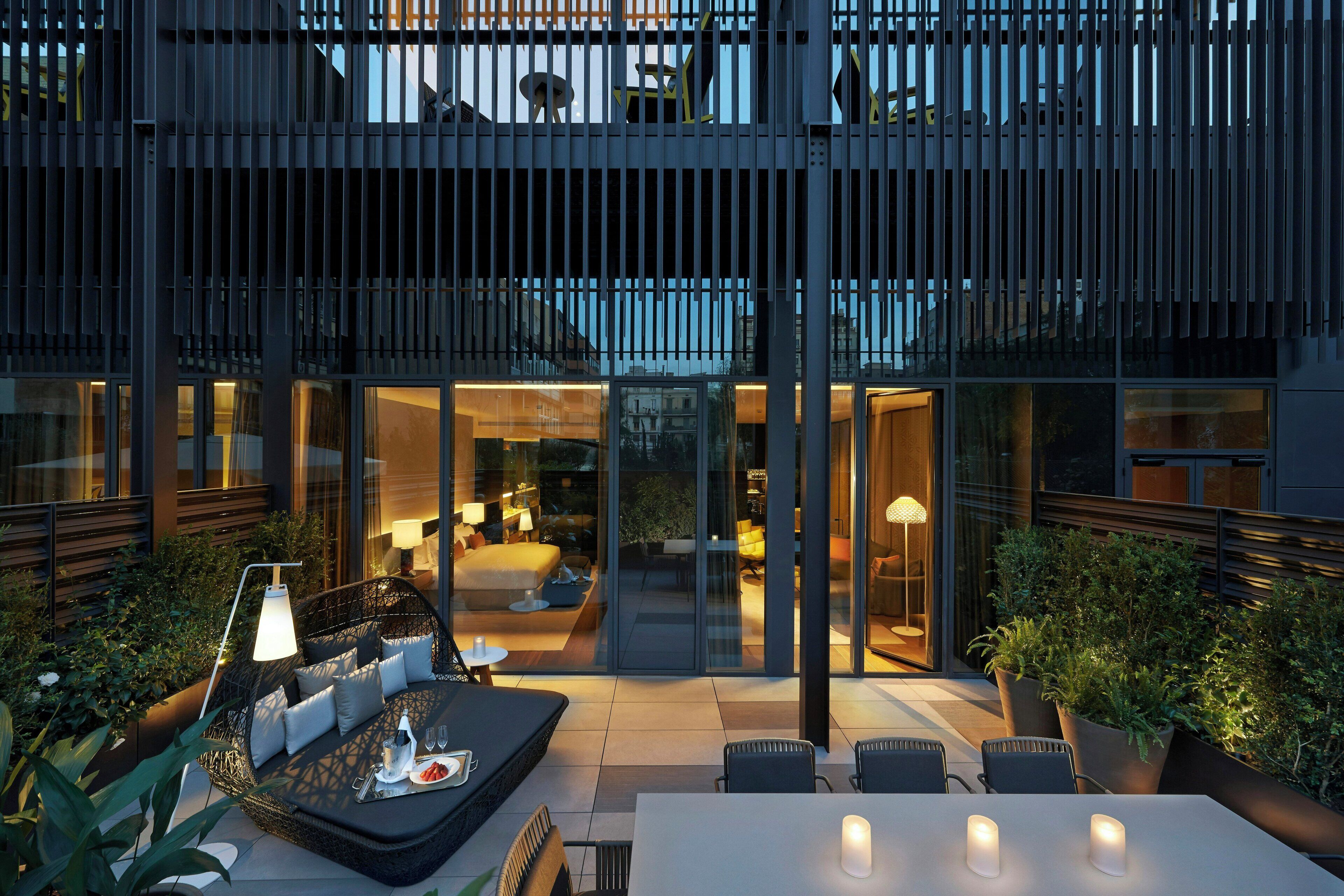 A modern outdoor patio area with seating and a dining table, surrounded by glass walls and potted plants.