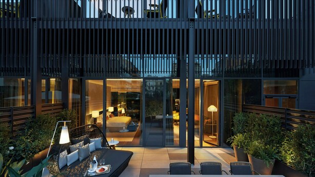 A modern outdoor patio area with seating and a dining table, surrounded by glass walls and potted plants.