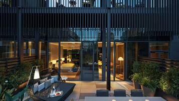 Un espace patio extérieur moderne, doté d’un coin salon et d’une table à manger, entouré de murs de verre et agrémenté de plantes en pot.