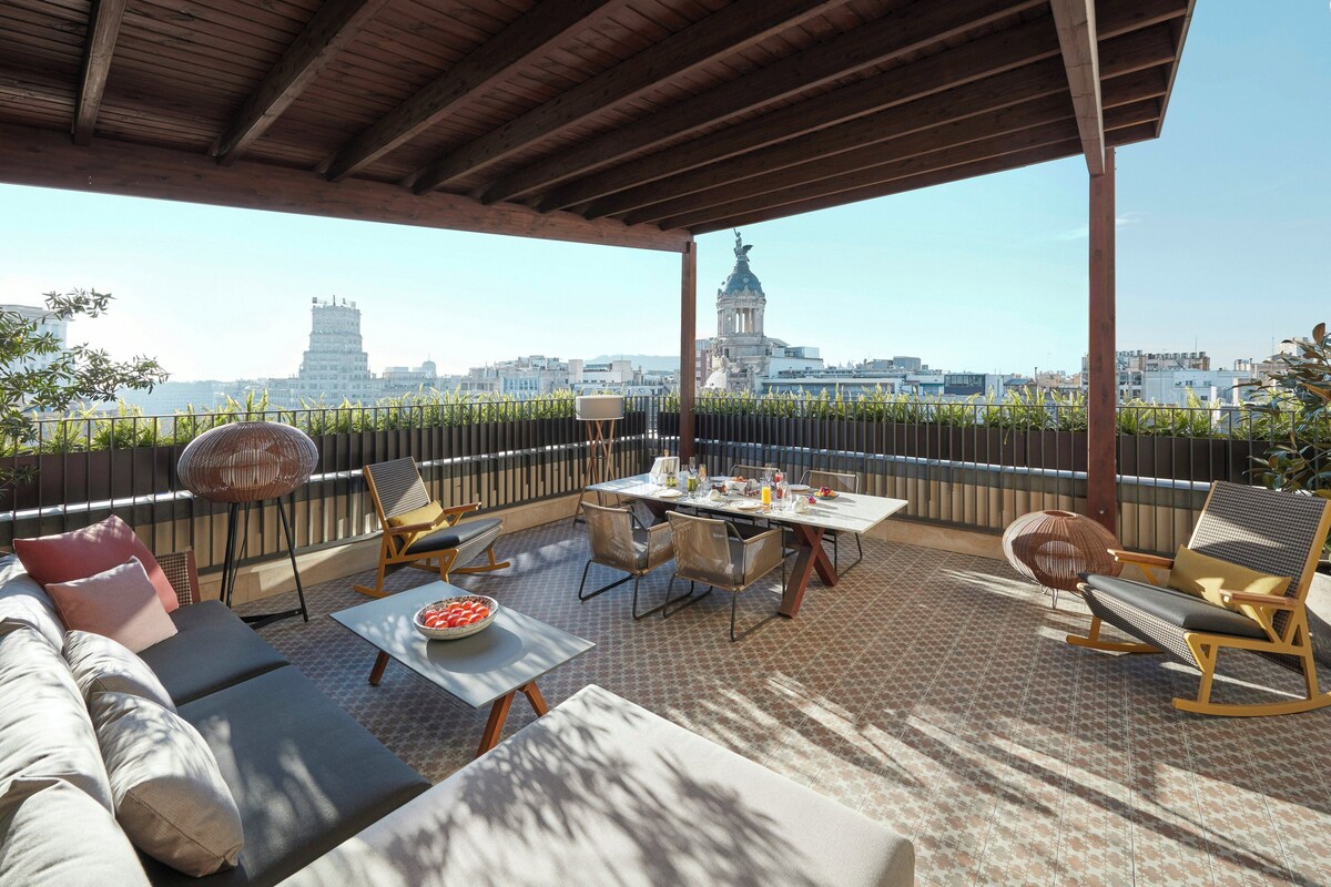 Una terraza en la azotea con una mesa de comedor para cuatro personas, rodeada de sillones y un sofá.