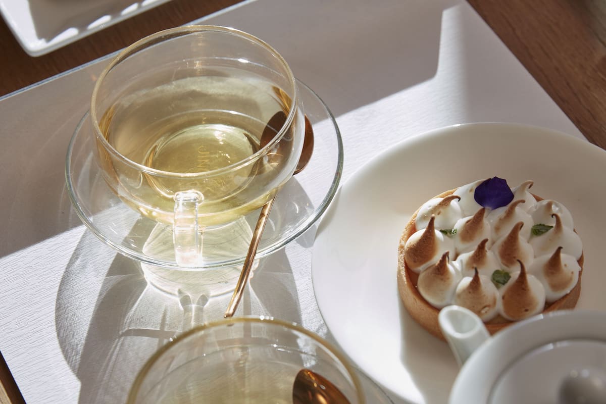 A table with a white plate containing a dessert, a glass of white beverage, and a small white container.