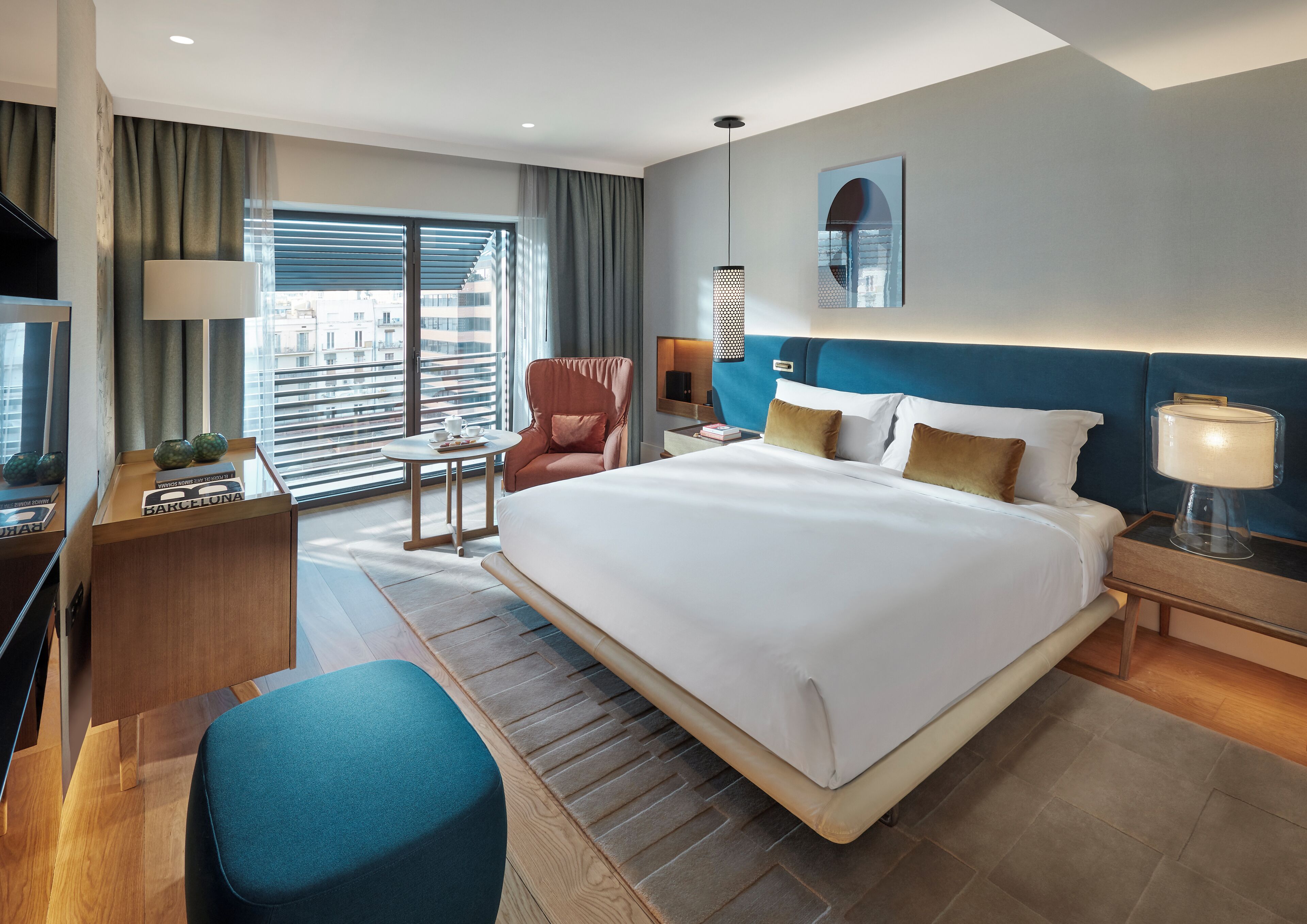 Ein Hotelzimmer mit einem großen Bett, einem Schreibtisch, einem Stuhl, einem Fernseher und einem Fenster mit Blick auf Gebäude.