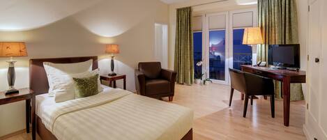 A hotel room with a bed, a desk, a chair, a TV, and a balcony with curtains.