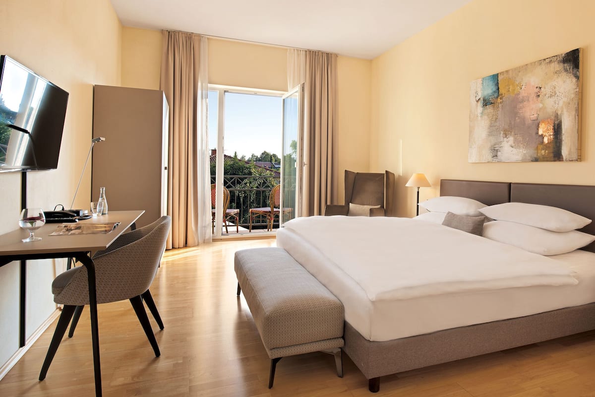 A hotel room with a bed, a desk with a chair, a television, and a painting on the wall.