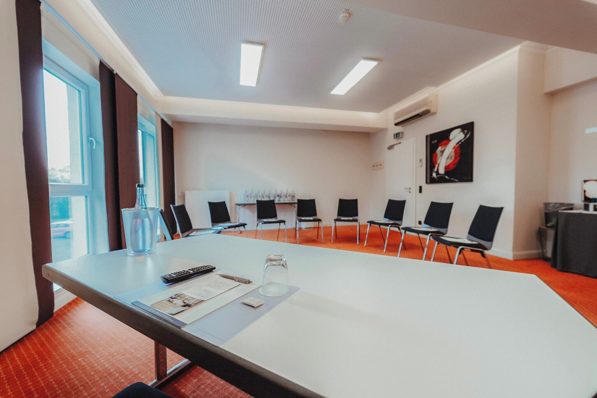 Un salón de conferencias con una larga mesa, sillas, una pantalla de proyector y un amplio ventanal.