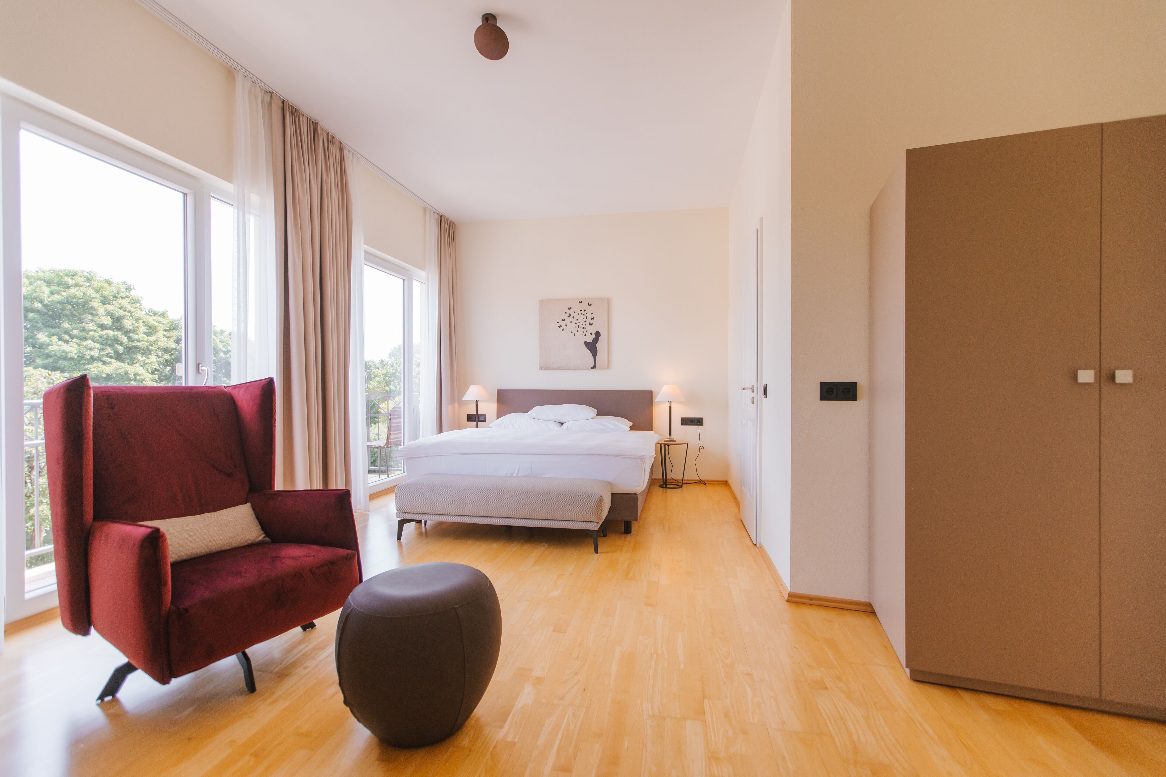 Un dormitorio moderno con una cama grande, un sillón rojo, un otoman redonda y un armario.