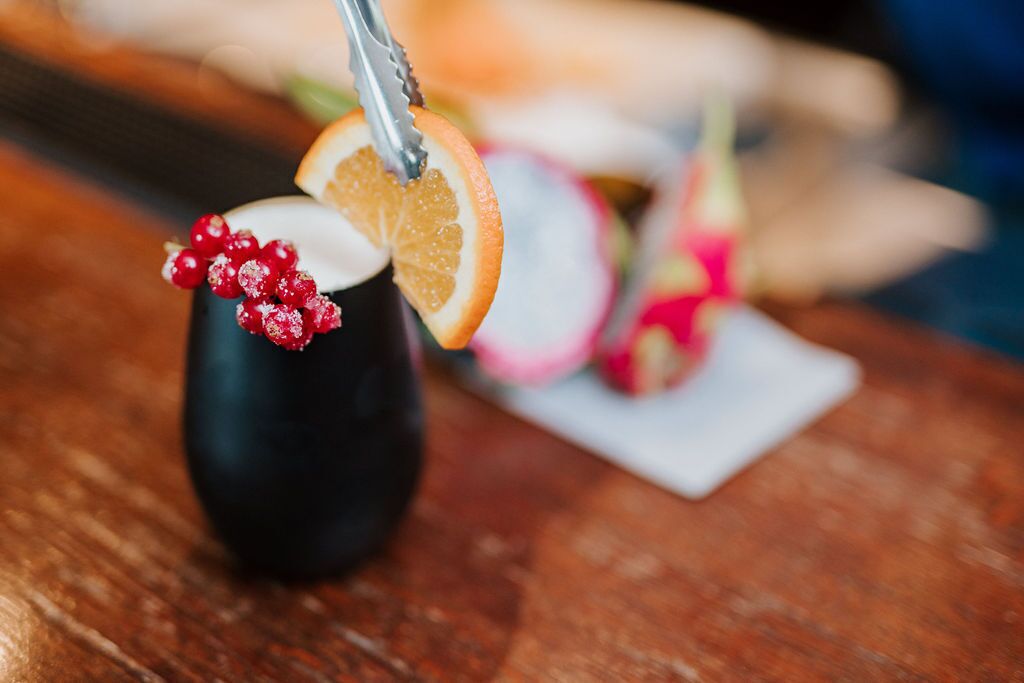 A dark-colored mug with a slice of orange and red berries on top.
