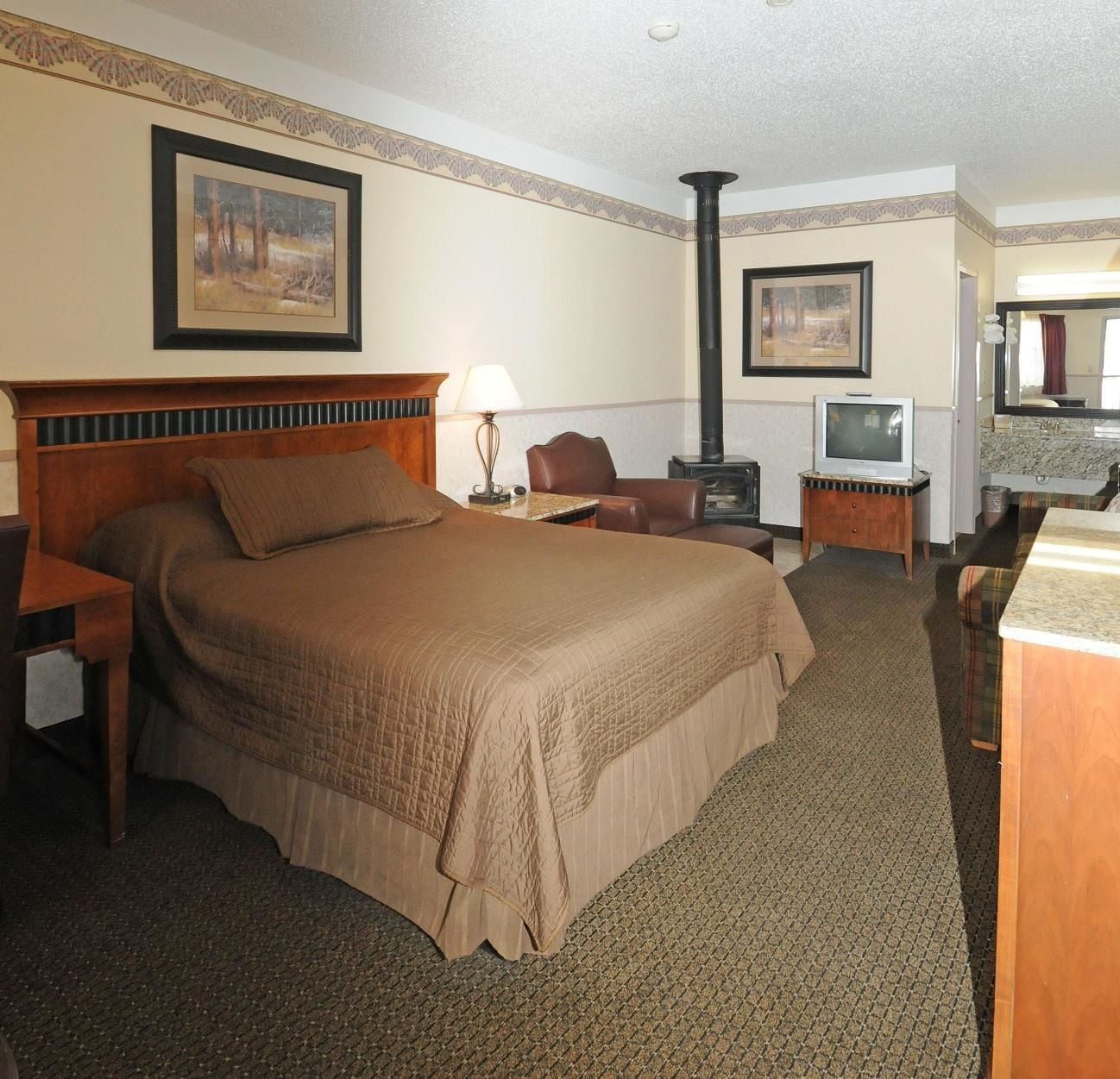 A hotel room with a large bed, a desk, a chair, a television, and a fireplace.