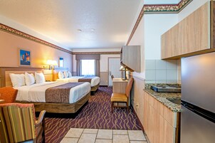 Quarto de hotel com duas camas, uma mesa, uma cadeira, uma cozinha compacta e um banheiro.
