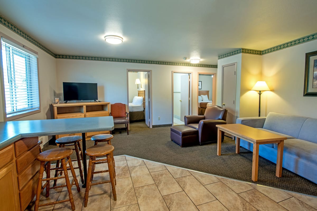 A spacious living area with a kitchen counter, bar stools, a sofa, and a television.