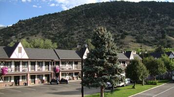 Un motel con estacionamiento, un área de estar techada al aire libre y montañas al fondo.