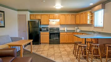 A compact kitchen with wooden cabinets, a refrigerator, a stove, and a sink. There are stools around the kitchen island.