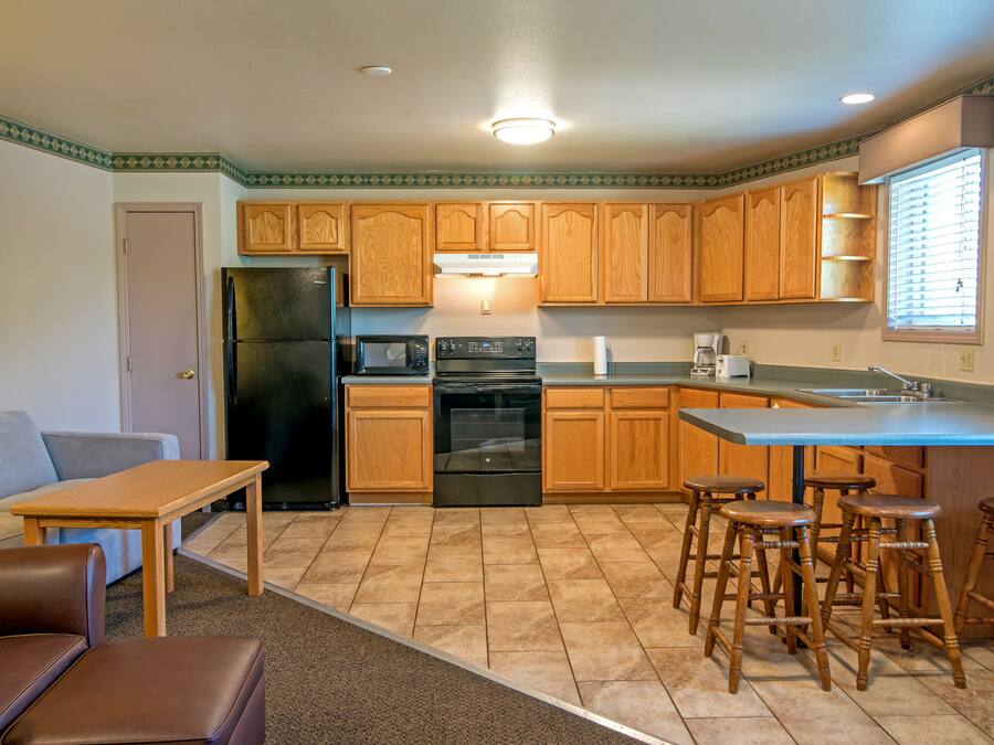 A compact kitchen with wooden cabinets, a refrigerator, a stove, and a sink. There are stools around the kitchen island.