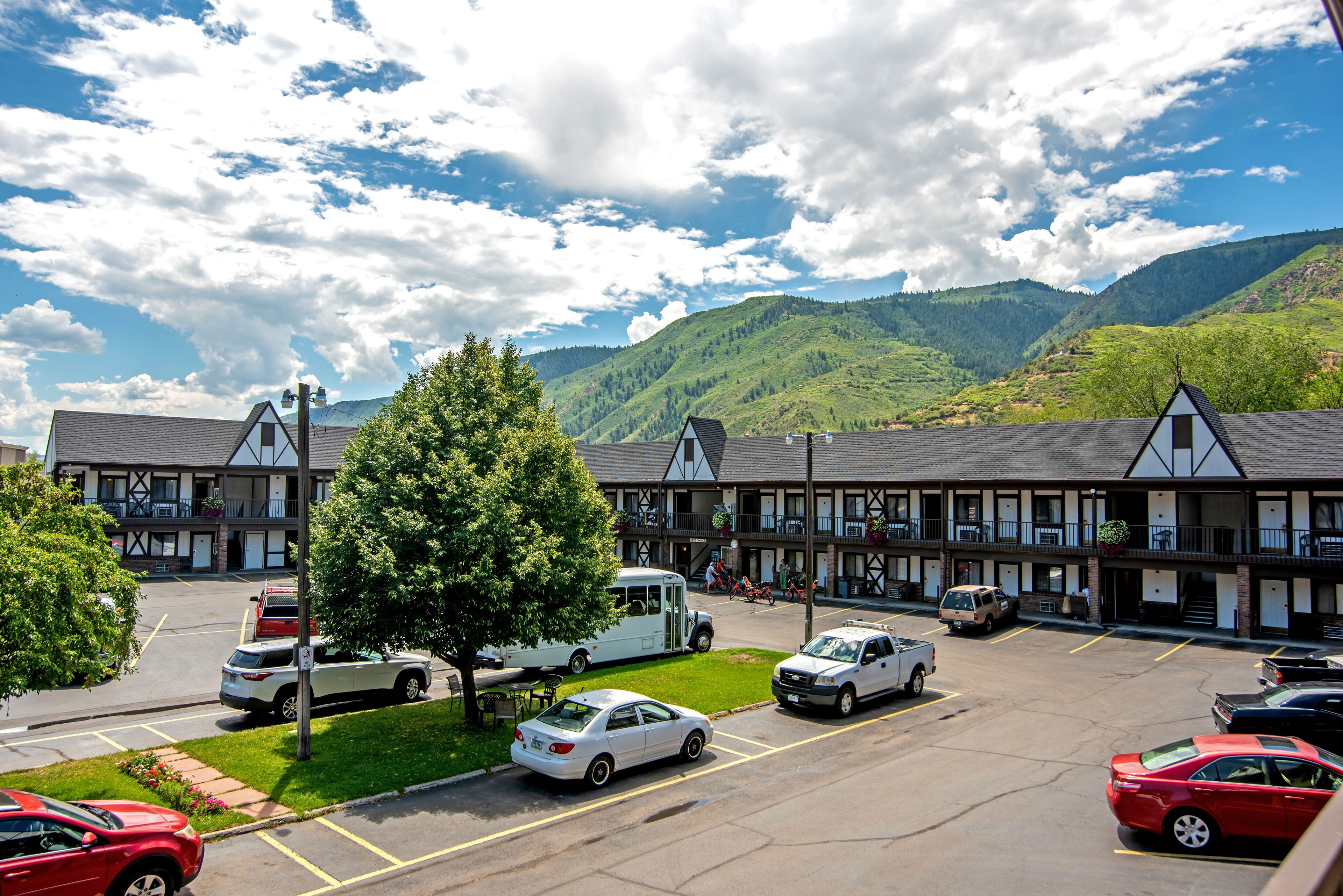 Un hotel con parcheggio, un albero grande e montagne sullo sfondo.