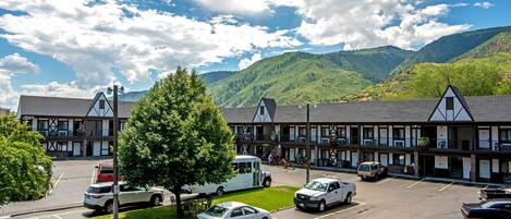 Un hotel con parcheggio, un albero grande e montagne sullo sfondo.