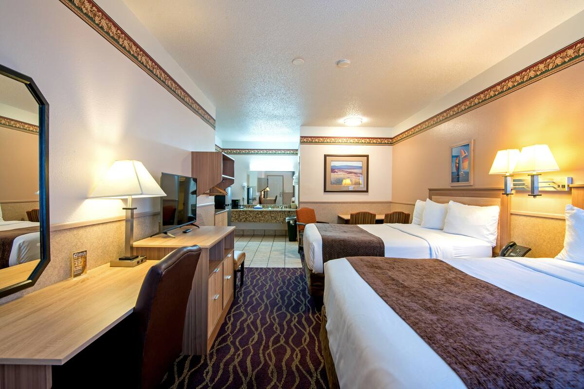 A hotel room with two beds, a desk, a chair, a mirror, and a bathroom visible in the background.