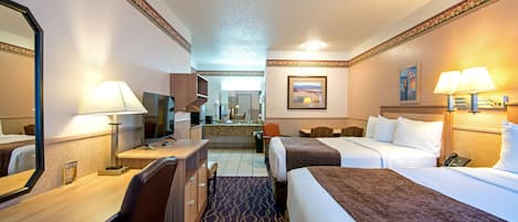 Quarto de hotel com duas camas, uma escrivaninha, uma cadeira, um espelho e um banheiro ao fundo.