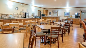 A spacious dining area with multiple wooden tables and chairs, a kitchen area with appliances, and a counter with various food items. - Silver Spruce Inn (Glenwood Springs)