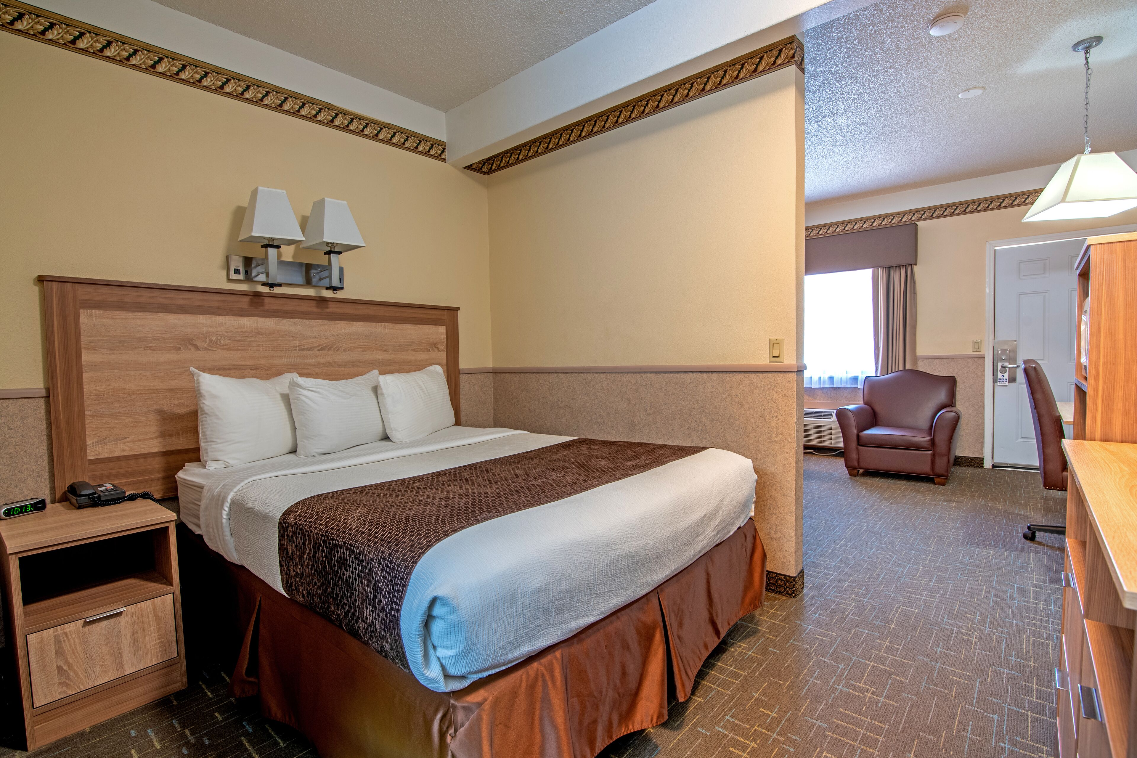 A hotel room with a large bed, bedside lamps, a wooden nightstand, a desk, and a chair.