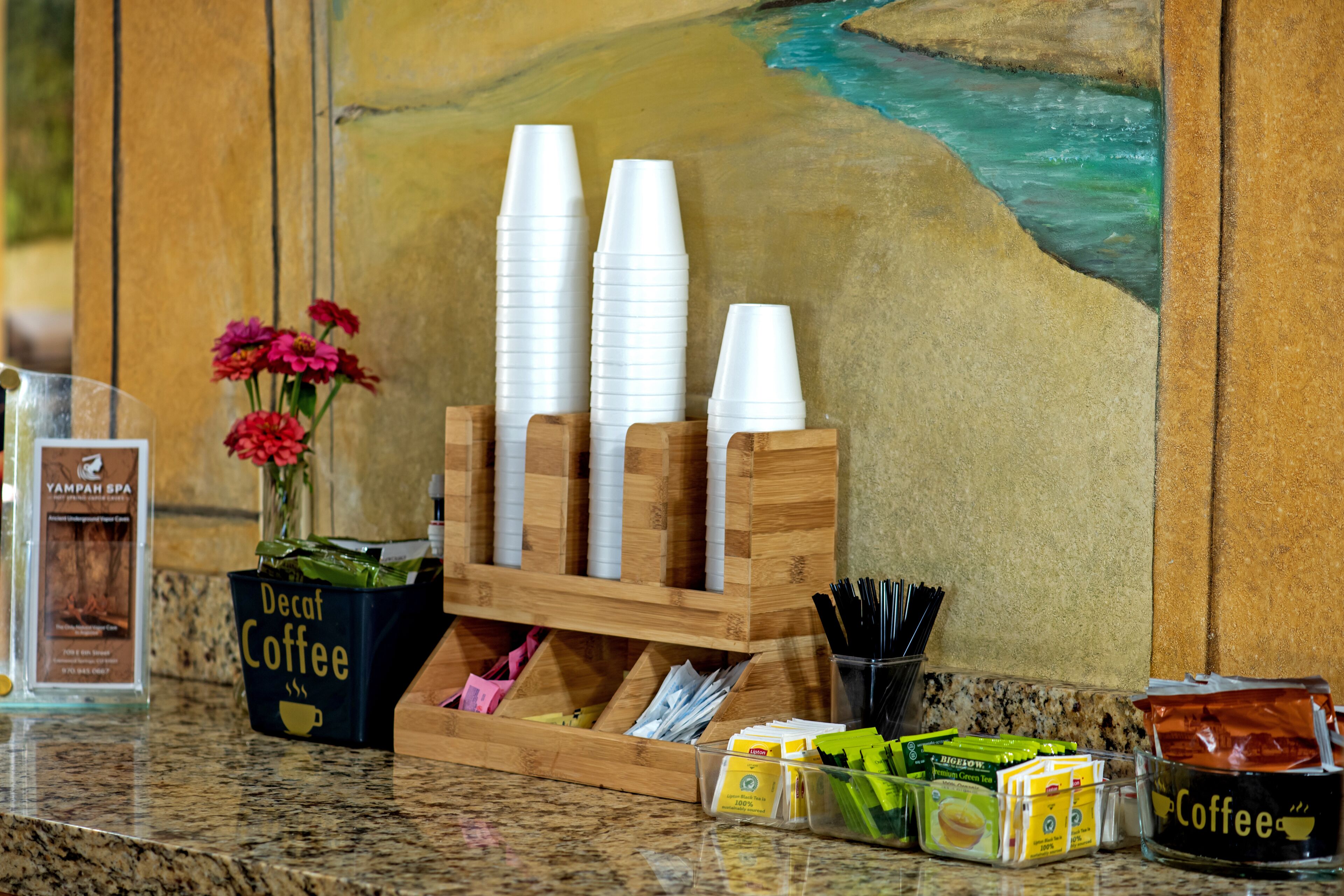 Una estación de café con vasos desechables, un porta tazas y diferentes productos de café sobre una encimera.