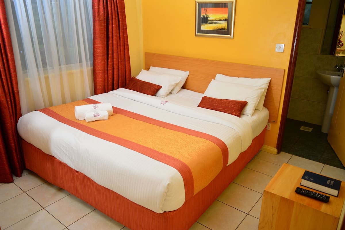 A double bed with white and orange bedding, a wooden headboard, and a framed picture on the wall.
