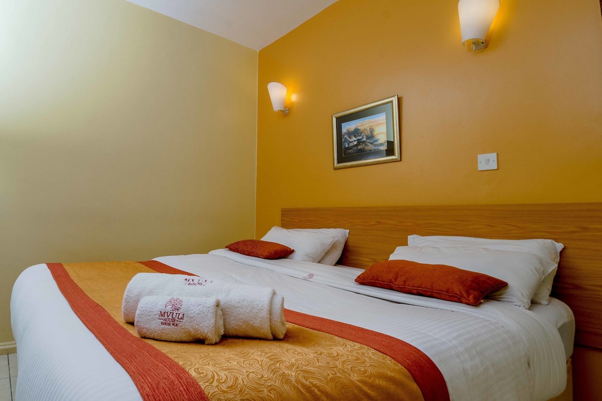 A hotel room with two beds, a painting on the wall, and a light fixture.