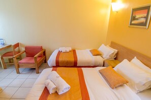 A hotel room with two beds, a wooden chair with a red cushion, and a small table with water bottles. - Mvuli House (Nairobi)