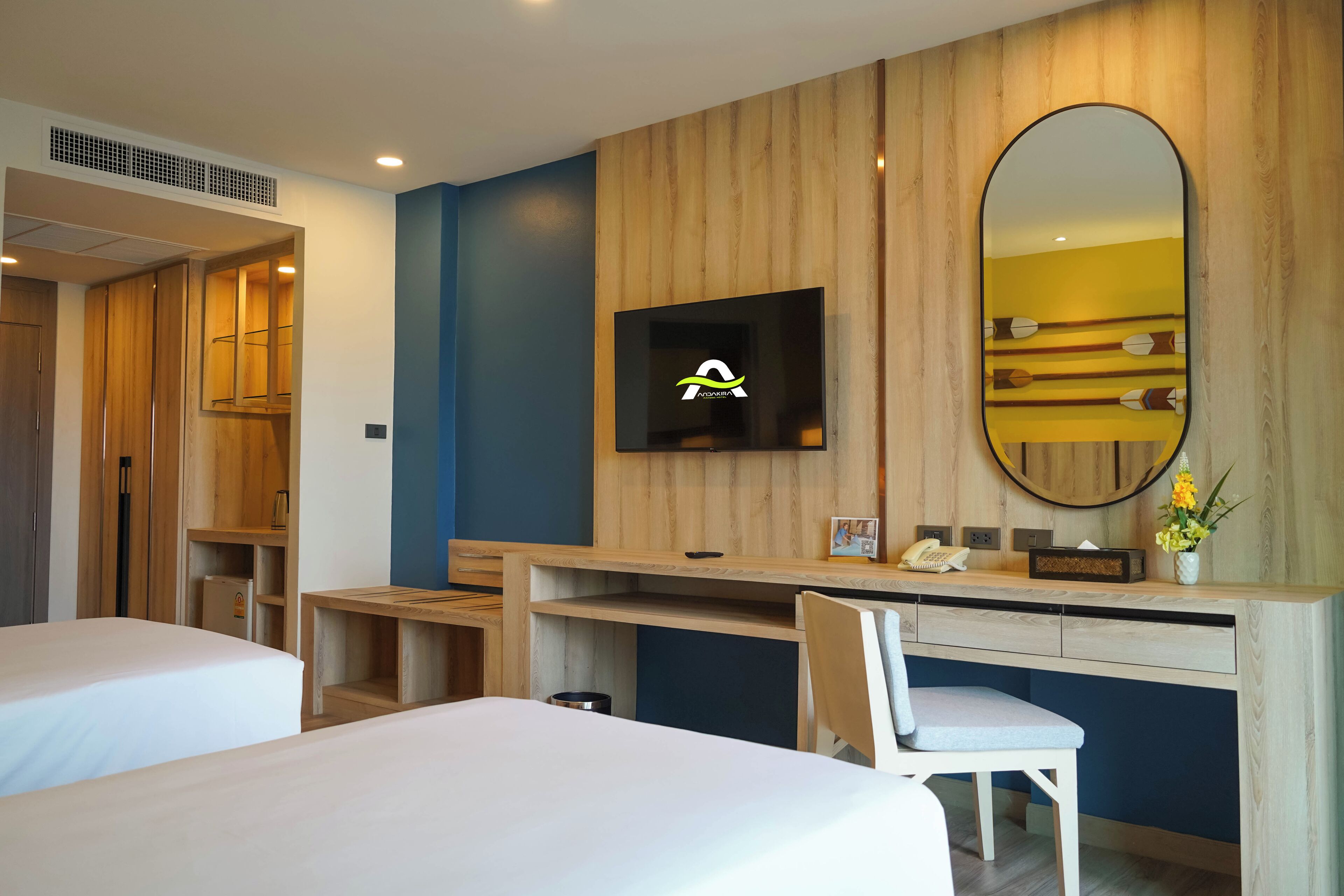 A hotel room with a bed, a desk with a chair, a television, and a large mirror.