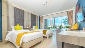 A hotel room with two beds, a desk, and a large window with a city view. - Andakira Hotel (Patong)