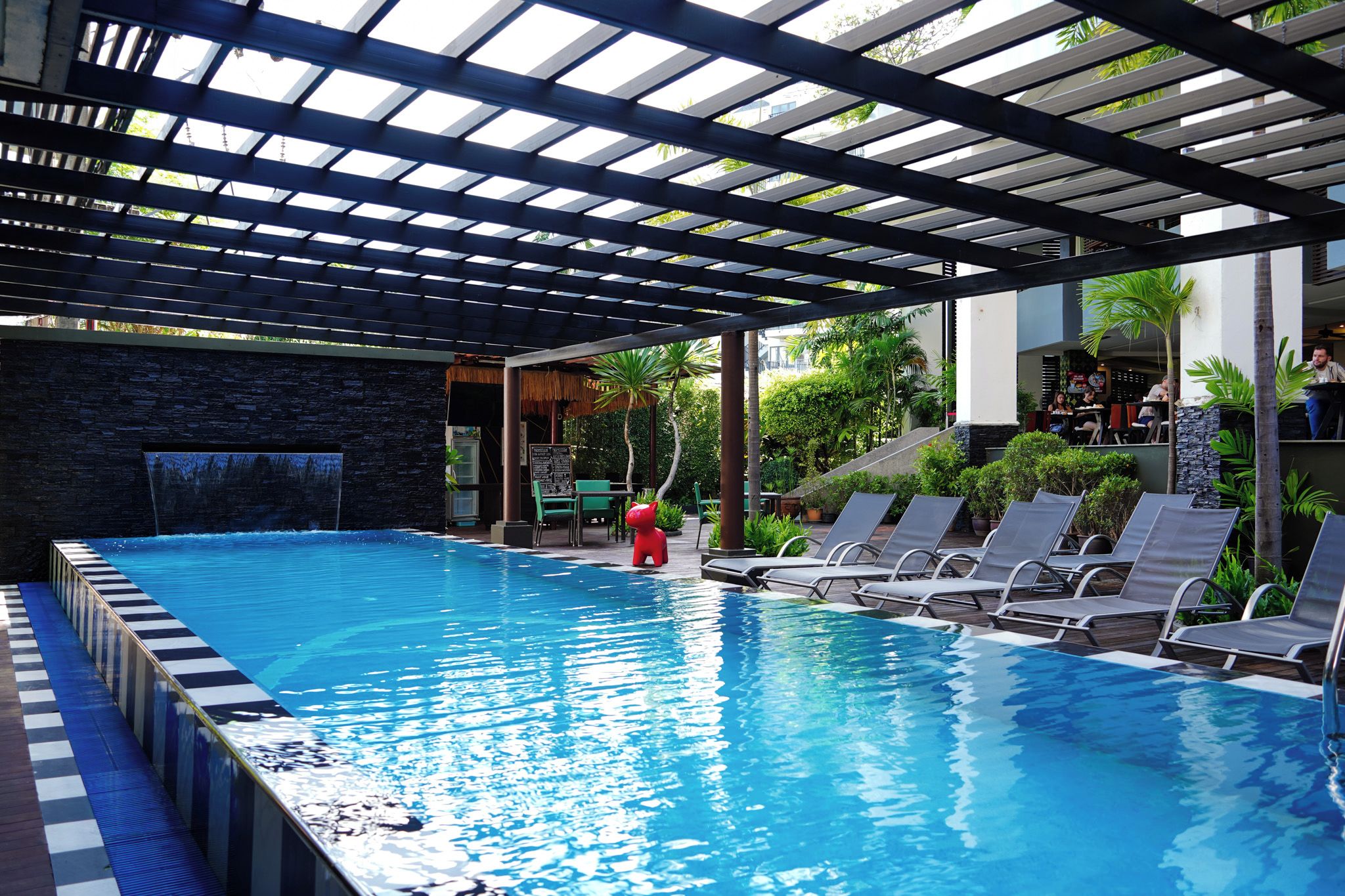 Piscina com pergolado, cadeiras de descanso e uma cascata.