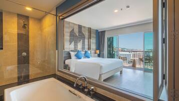 A modern hotel room with a large bed, a bathtub, and a balcony with a view.