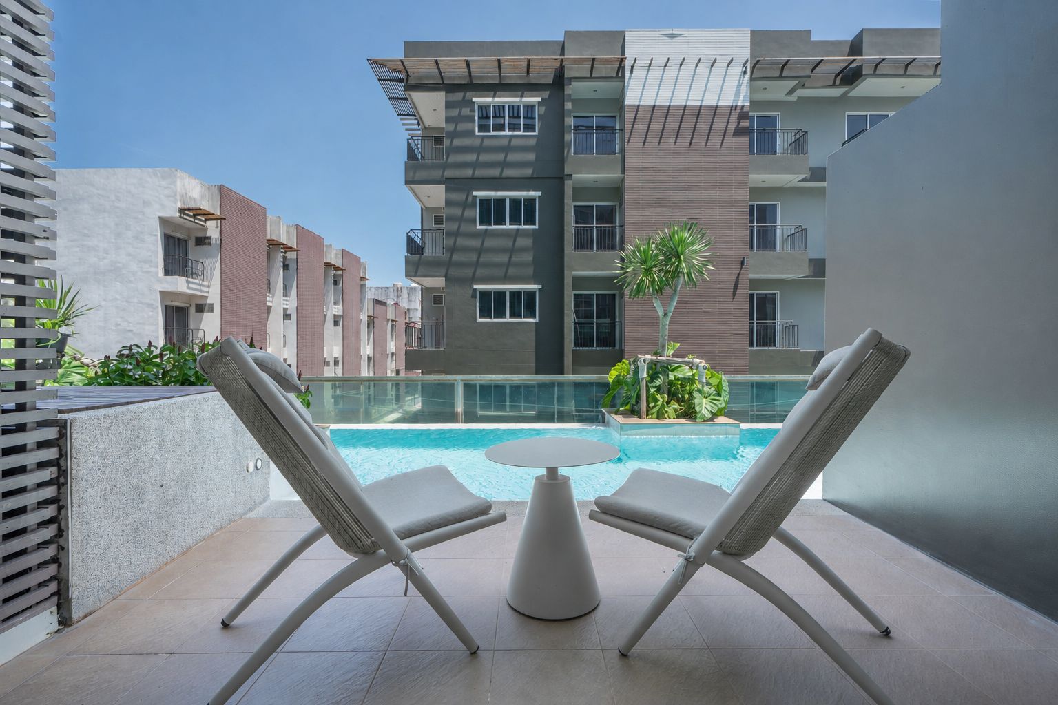 A modern outdoor pool area with lounge chairs and a table, surrounded by a high-rise building with balconies.