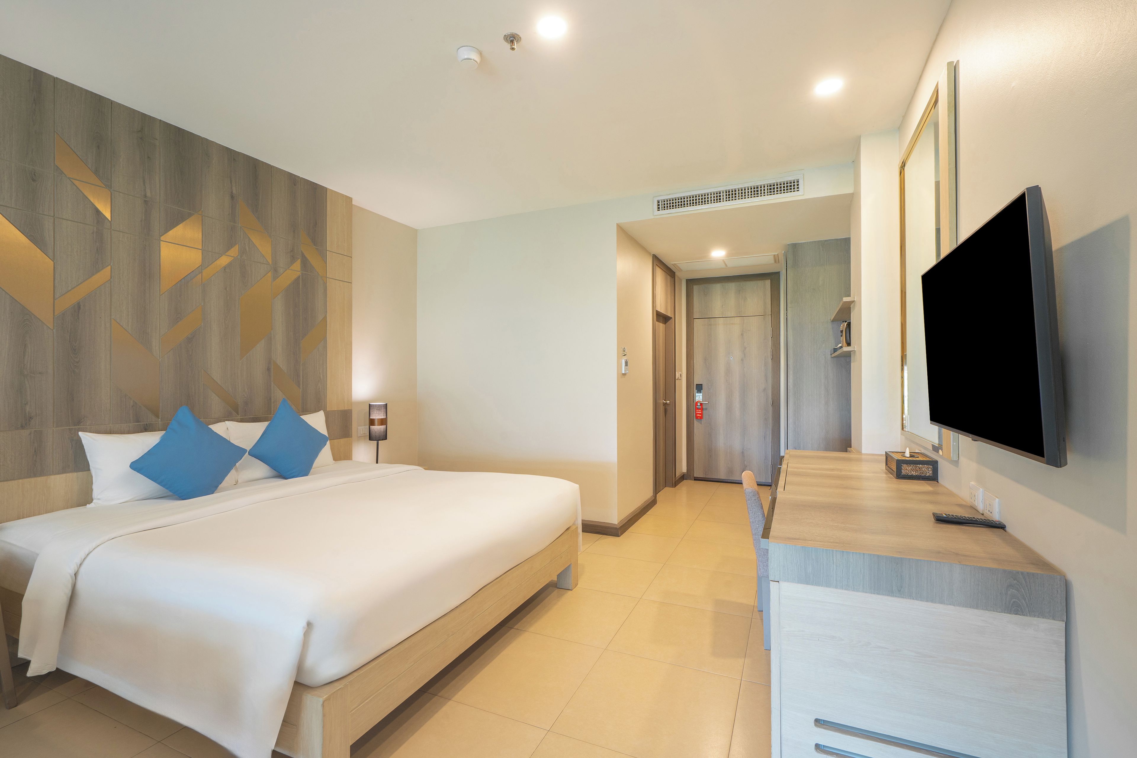 A hotel room with a bed, a TV, a desk, and a bathroom door.