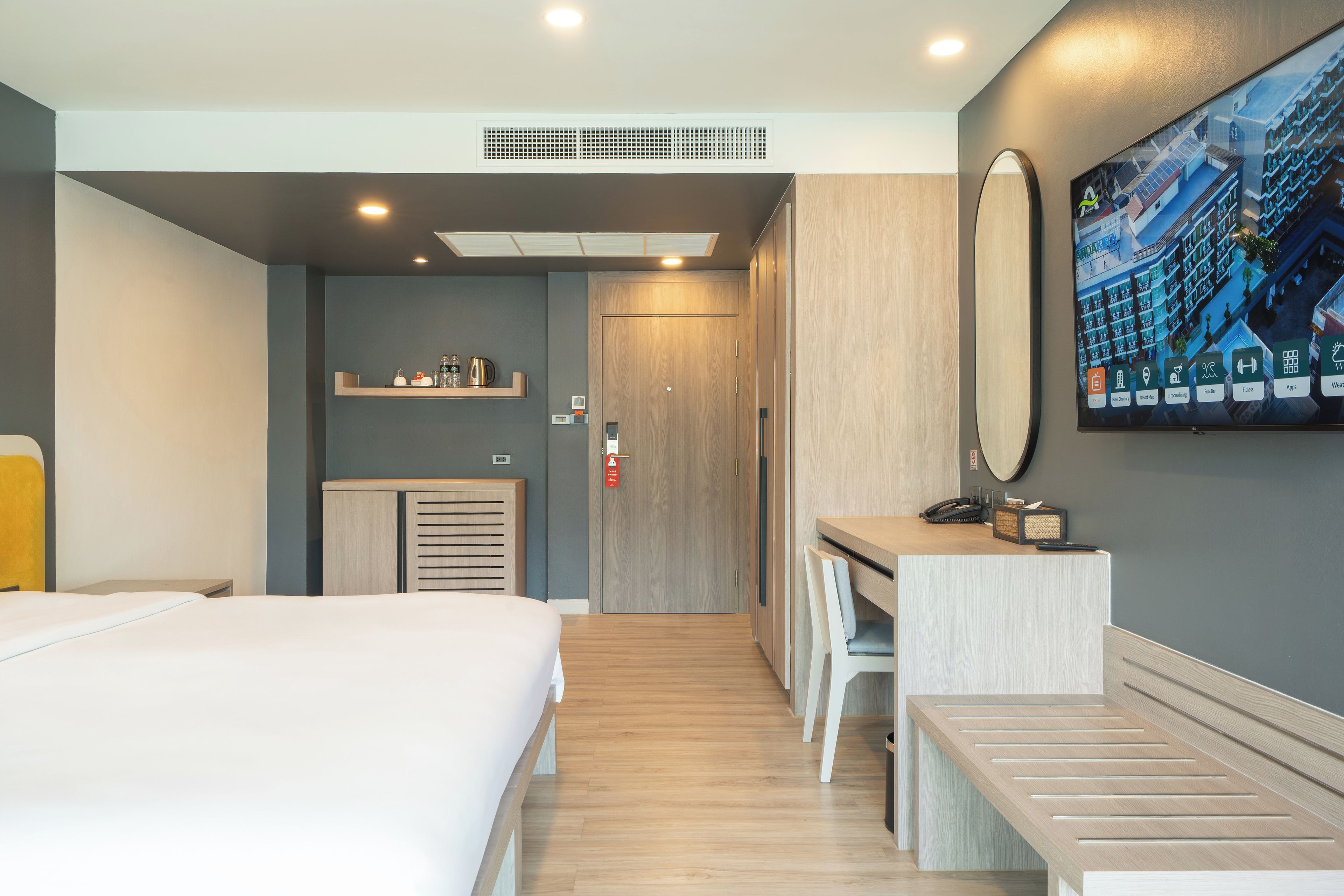 A hotel room with a bed, a desk, a mirror, and a television displaying hotel amenities.