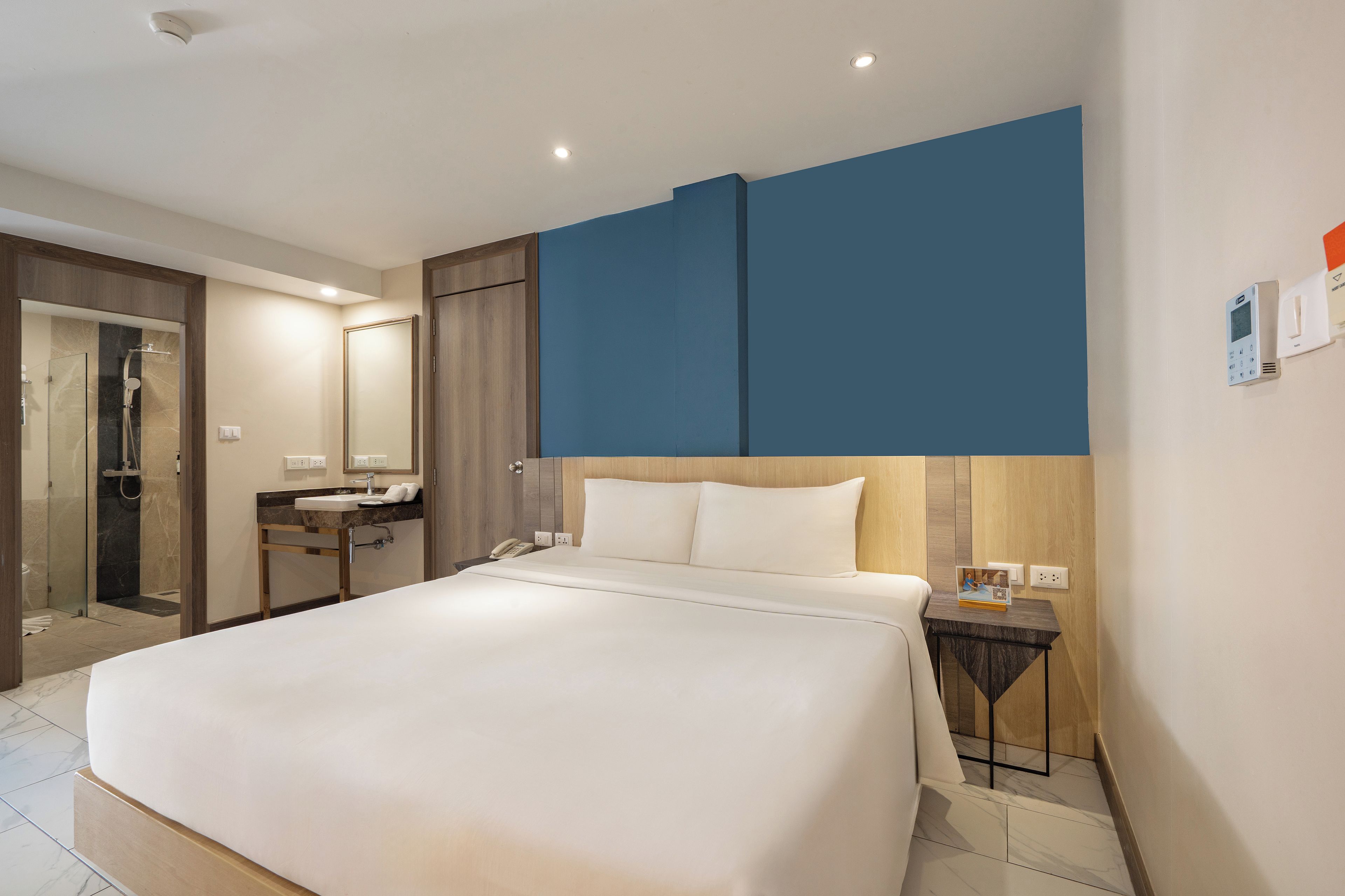 Habitación de hotel con cama, baño con ducha y mesita de noche con teléfono y un pequeño marco de fotos.