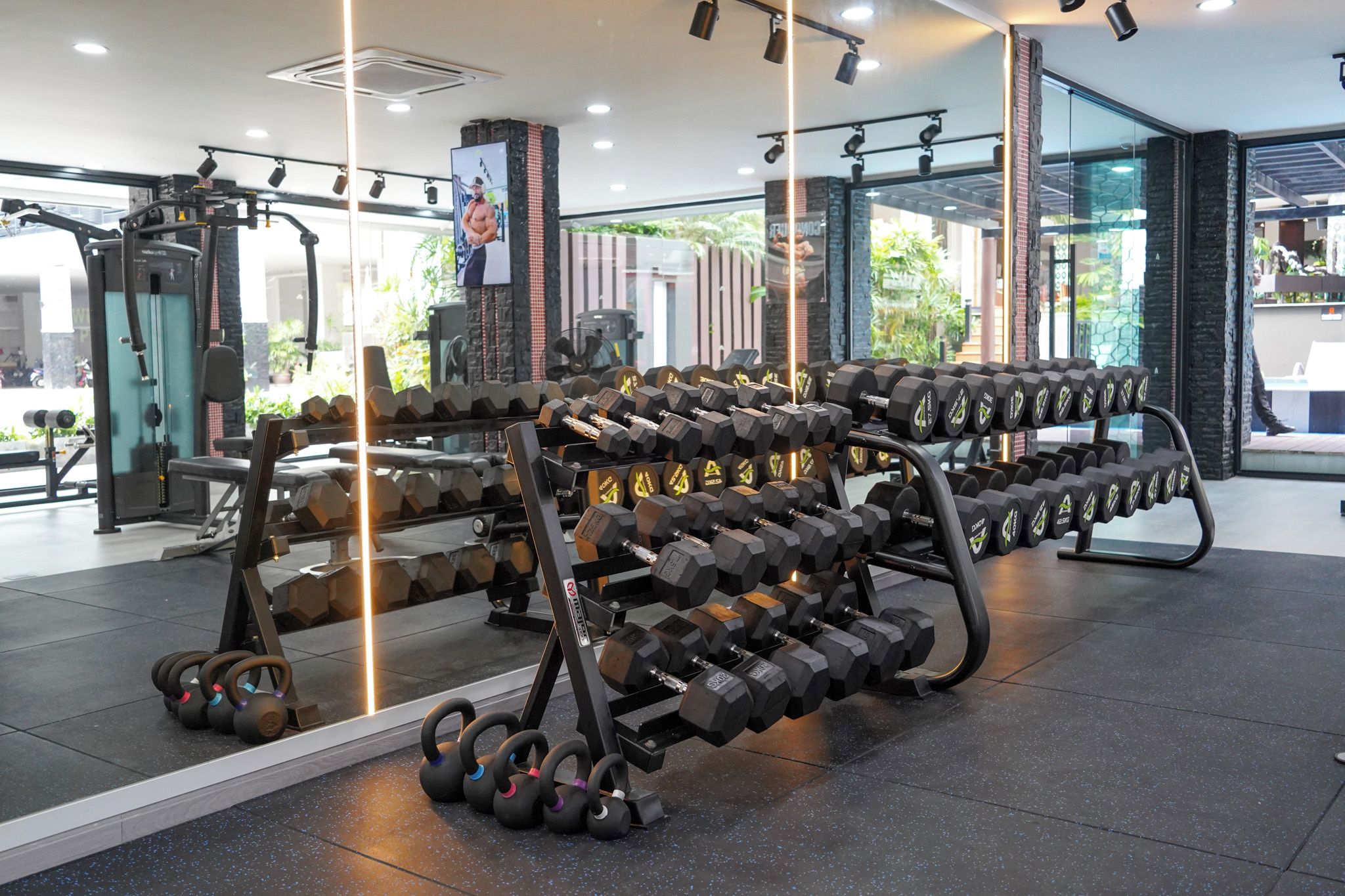 A gym with various weightlifting equipment, including dumbbells and kettlebells, arranged on racks.