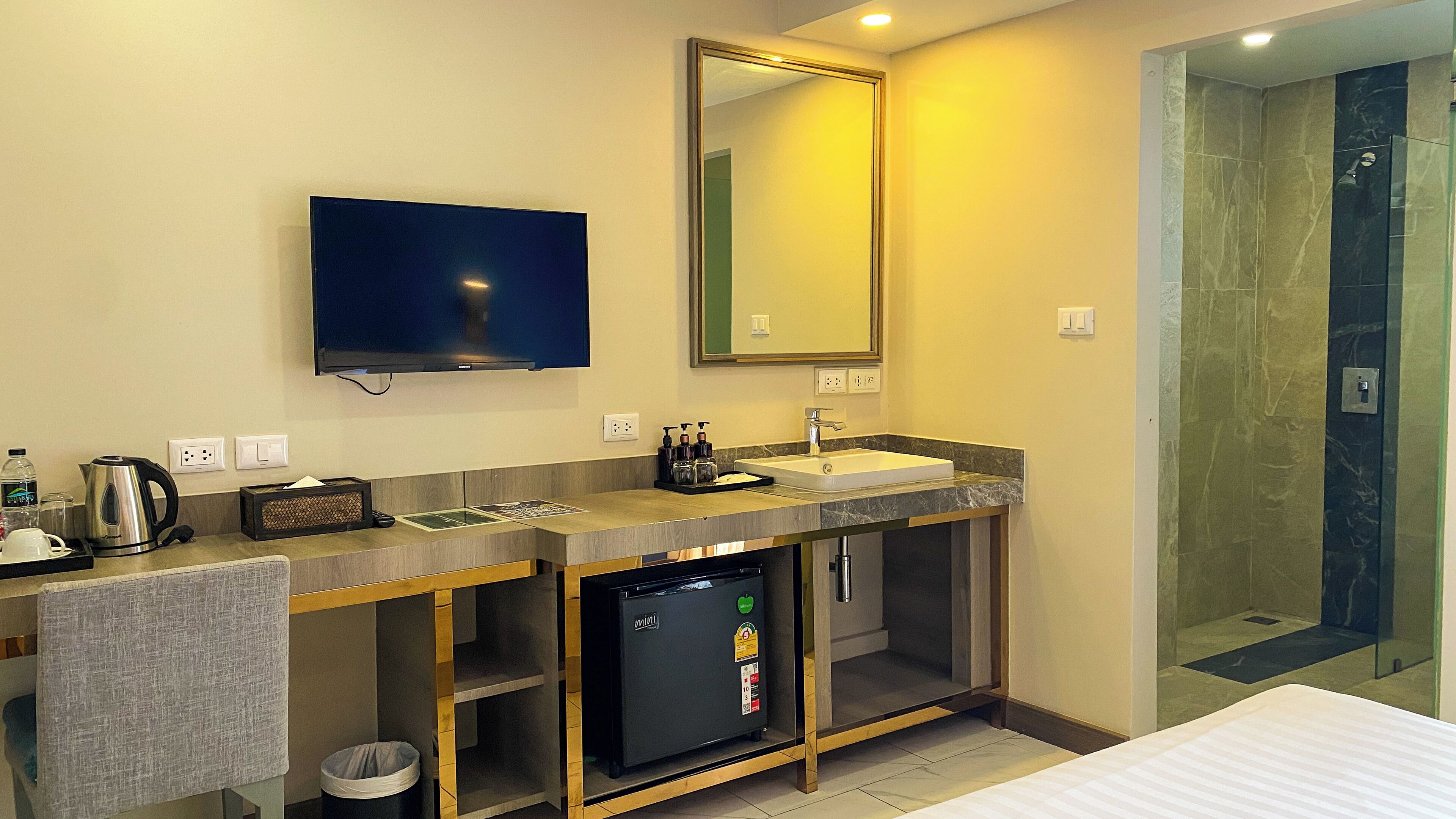 Un bagno moderno con lavandino, specchio, televisione e cabina doccia.
