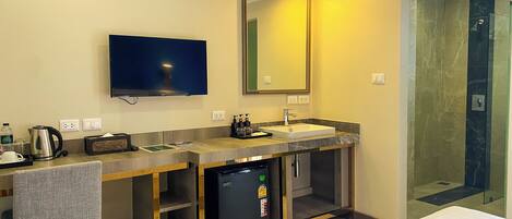 Un bagno moderno con lavandino, specchio, televisione e cabina doccia.