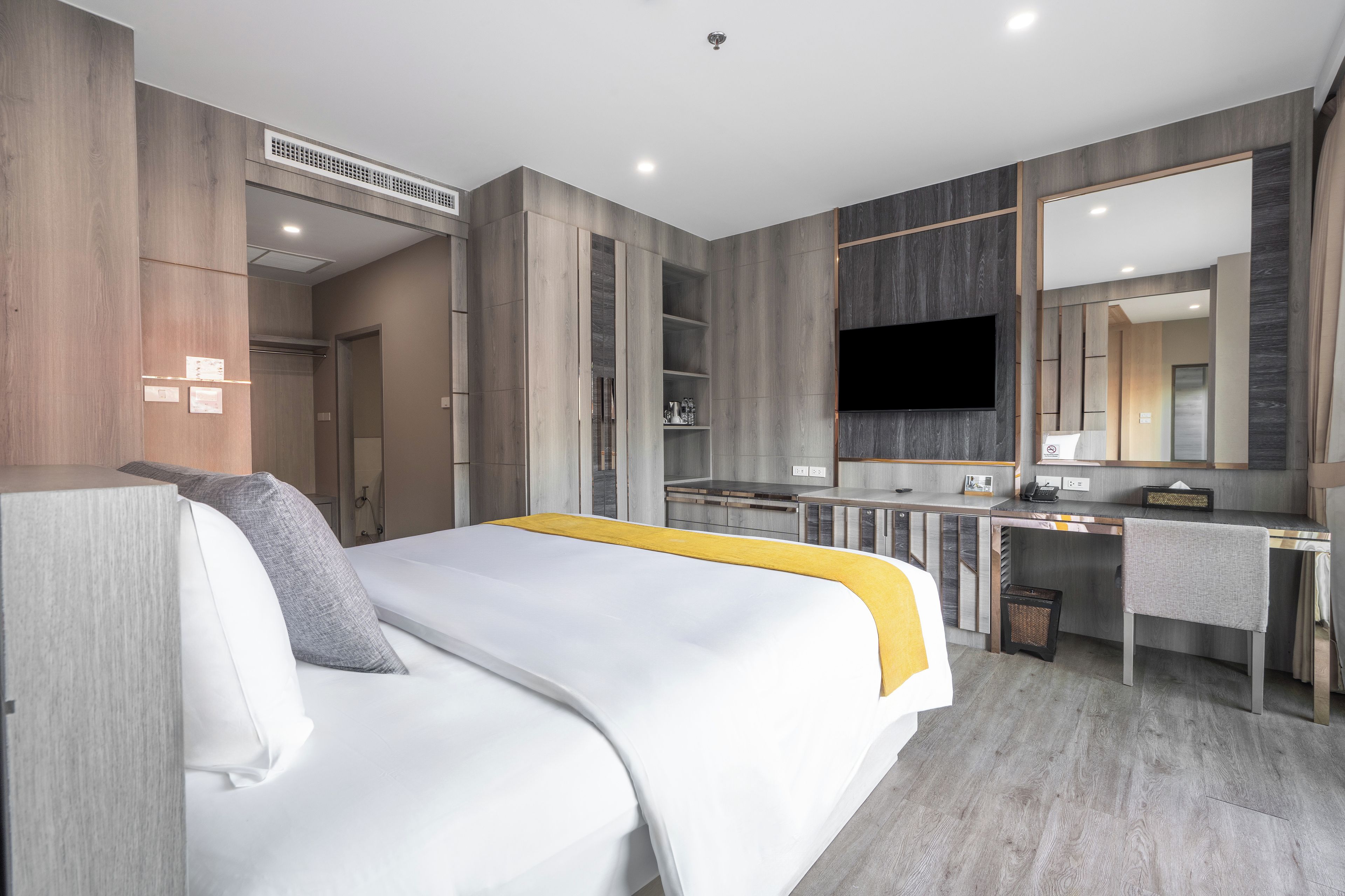 A modern hotel room with a bed, a desk, a television, and a large mirror.
