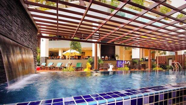 An indoor swimming pool with a tiled edge, a waterfall feature, and lounge chairs. - Andakira Hotel (Patong)